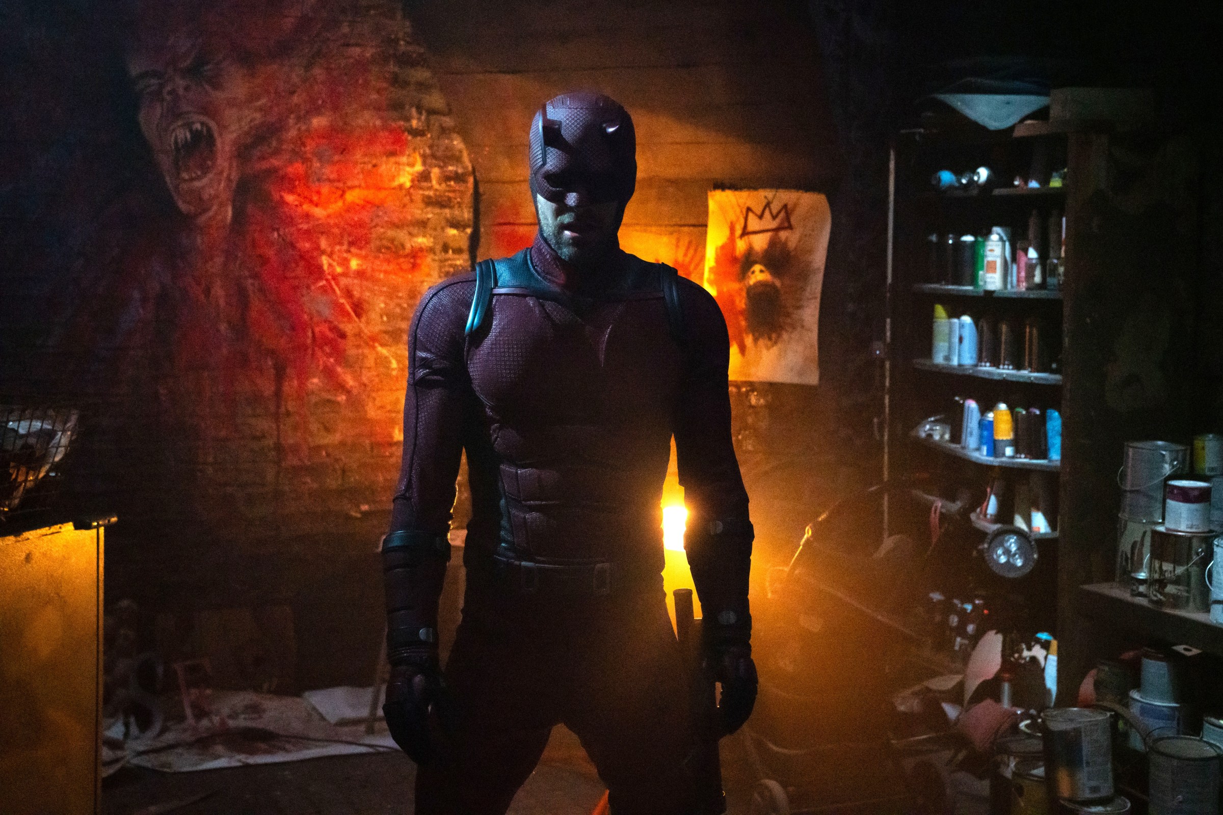 Daredevil/Matt Murdock stands in a dark and grimy room where the walls are covered in drawings of screaming an mutilated faces in Daredevil: Born Again.